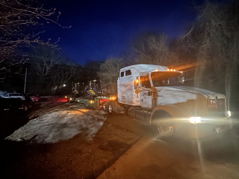 Night-time recovery hauling skid steers on a lowboy trailer